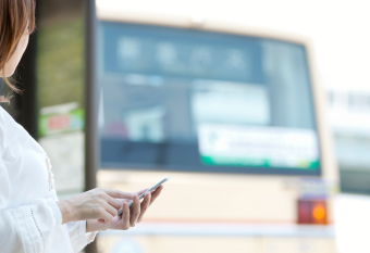 バス停でスマートフォンを操作する女性